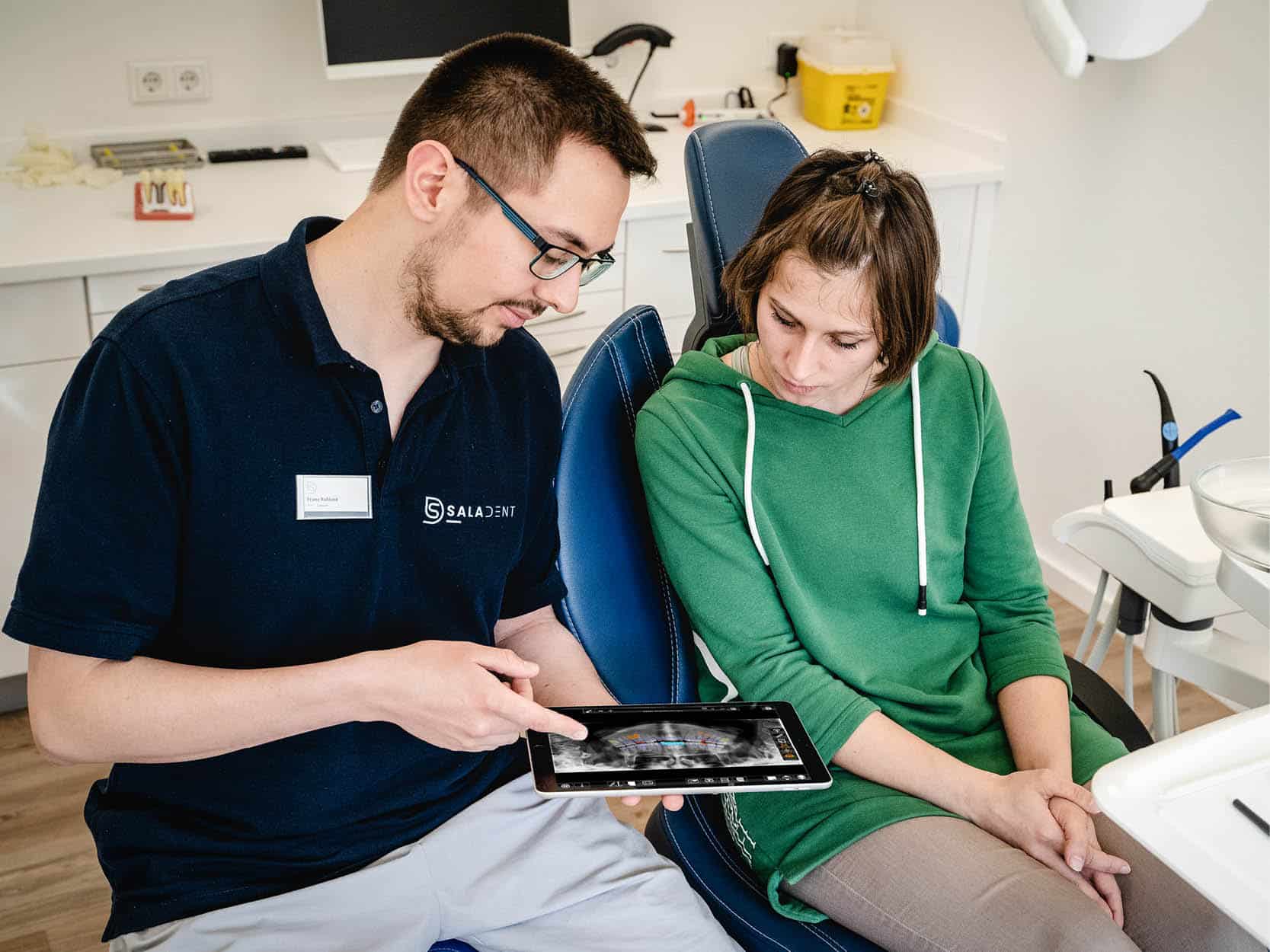 Zahnarzt Dr. Ruhland zeigt Patientin ein Röntgenbild auf dem iPad