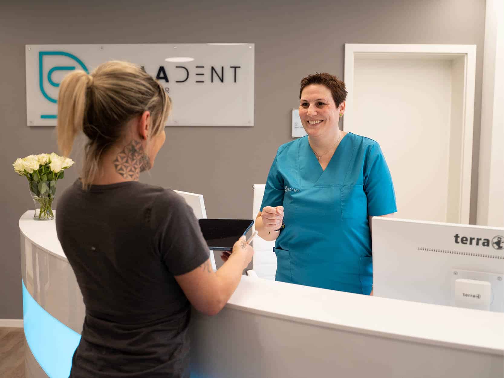 Zahnarzthelferin begrüßt freundlich eine Patientin am Empfangstresen